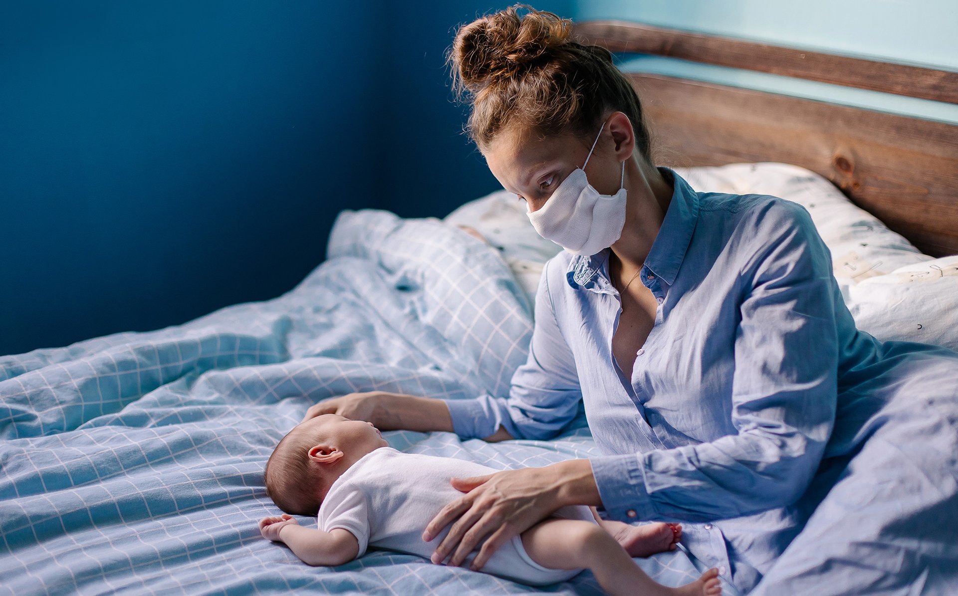 Mama w maseczce lezy z dzieckiem na lozku